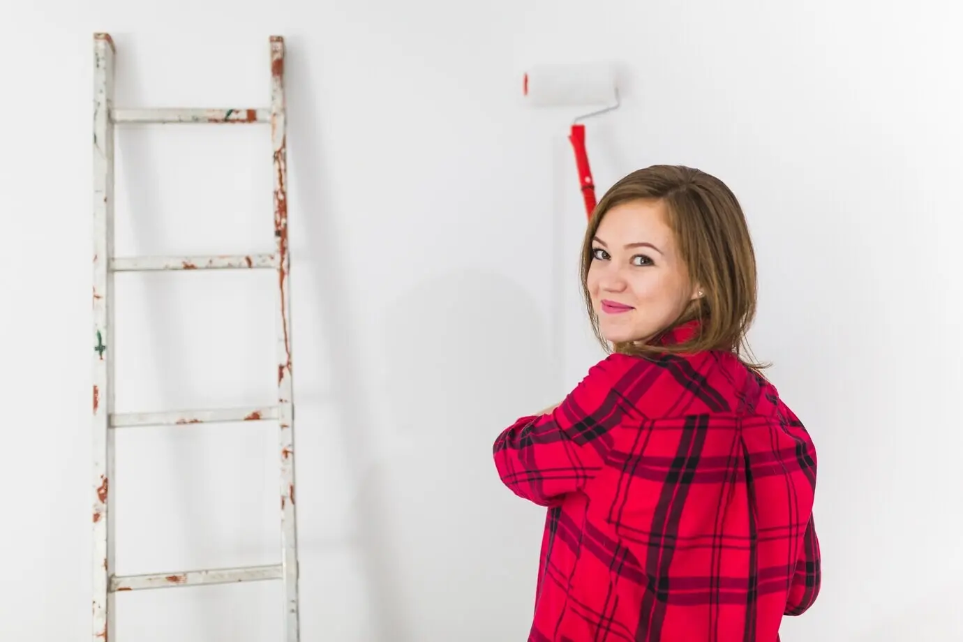 Eine niedliche Frau streicht eine Wand mit einer Rolle.